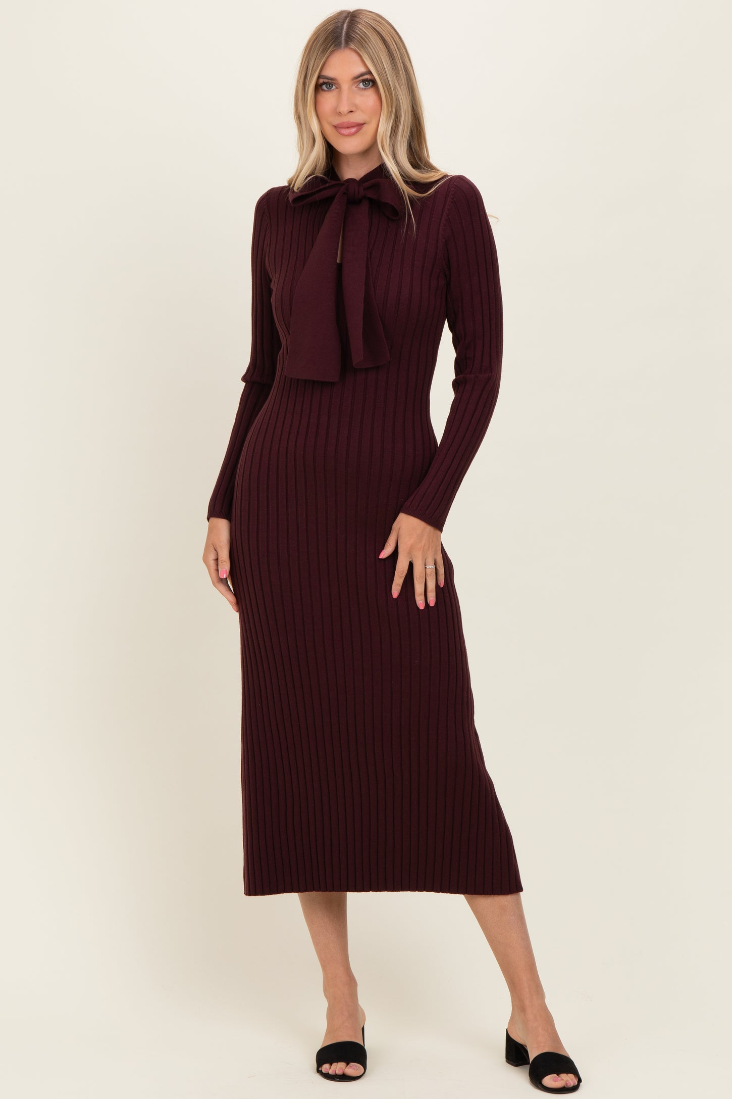 woman wearing a burgundy ribbed midi dress with a tie detail at the neckline and long sleeves