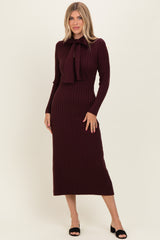 woman wearing a burgundy ribbed midi dress with a tie detail at the neckline and long sleeves