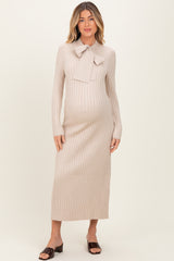 woman wearing a light beige maternity sweater dress with a bow tie detail and long sleeves, showing her baby bump