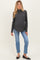 woman wearing a dark gray maternity sweater with a high neckline and blue jeans, showing a visible baby bump