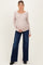 woman wearing a beige long sleeve maternity top and blue wide leg maternity jeans, holding her baby bump