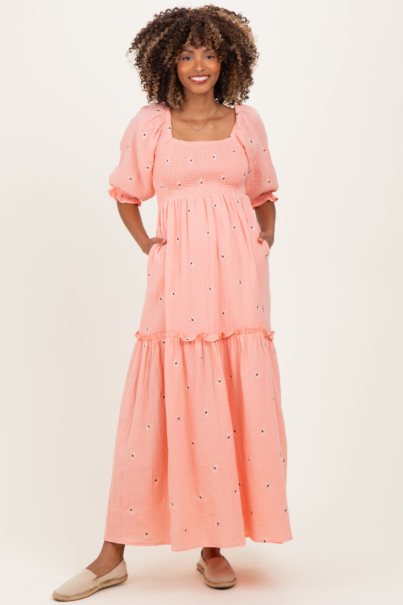woman wearing a light pink maternity maxi dress with puff sleeves and floral embroidery