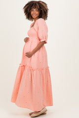 woman wearing a coral maternity maxi dress with a tiered skirt and puff sleeves, holding her baby bump