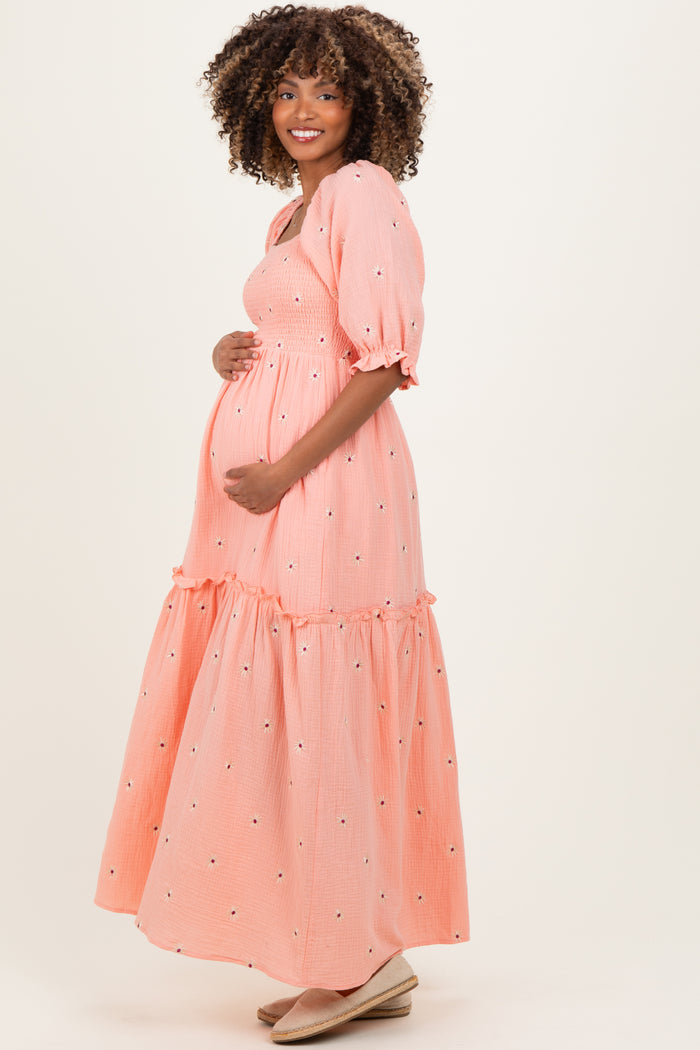 woman wearing a coral maternity maxi dress with a tiered skirt and puff sleeves, holding her baby bump