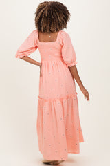 woman wearing a pink maternity maxi dress with puff sleeves and floral accents, showing a relaxed fit at the back
