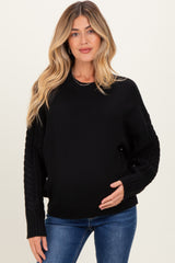 woman wearing a black maternity sweater with cable knit sleeves, holding her baby bump