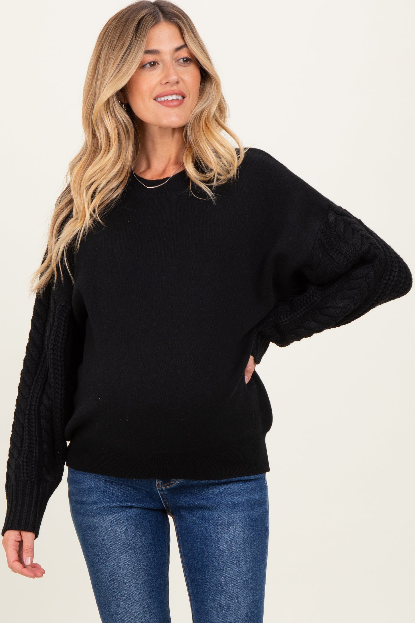 woman wearing a black maternity sweater with cable knit sleeves and a visible baby bump