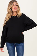 woman wearing a black maternity sweater with cable knit sleeves and a visible baby bump