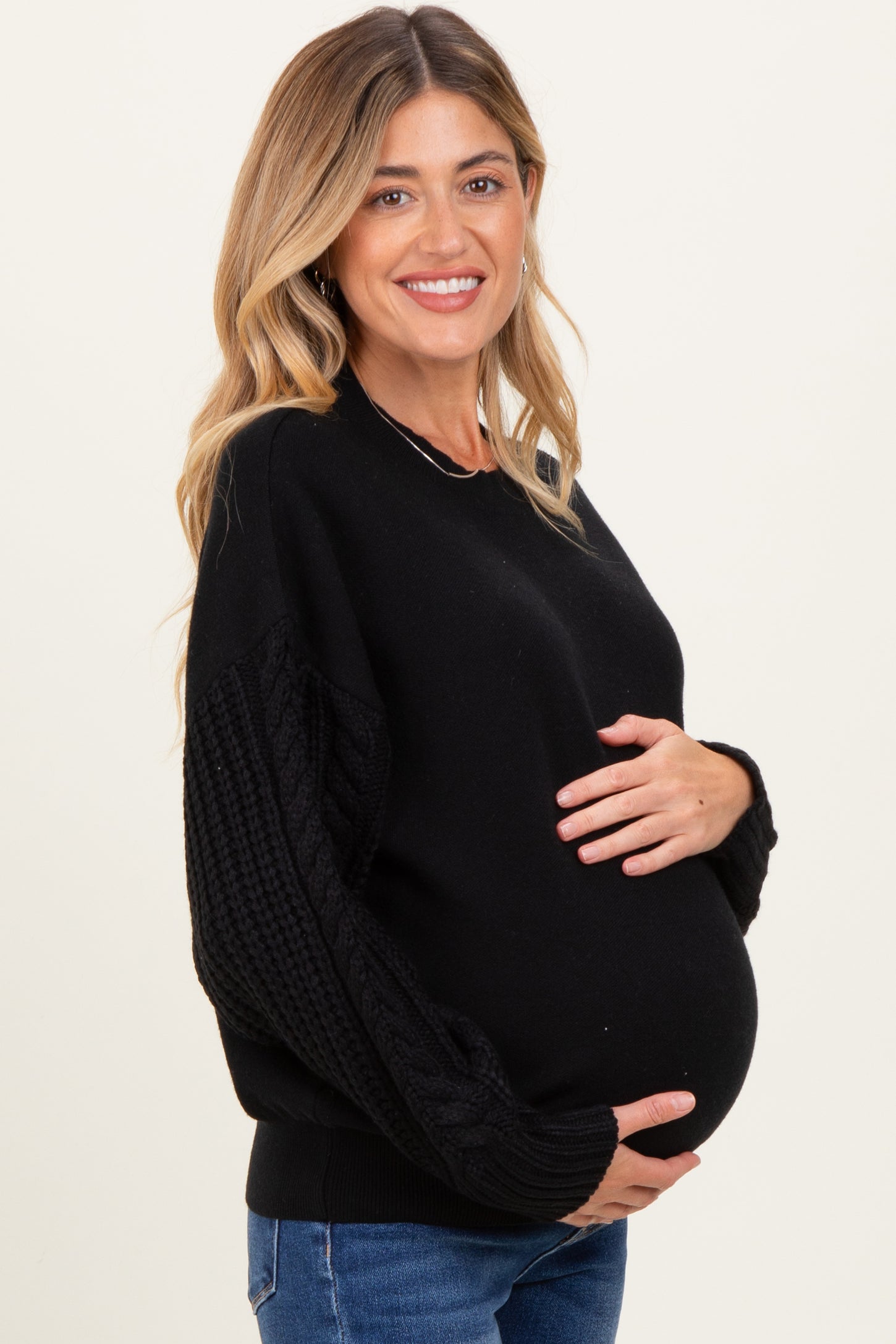 woman wearing a black maternity sweater with textured sleeves and holding her baby bump