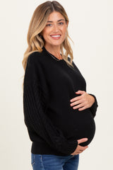 woman wearing a black maternity sweater with textured sleeves and holding her baby bump