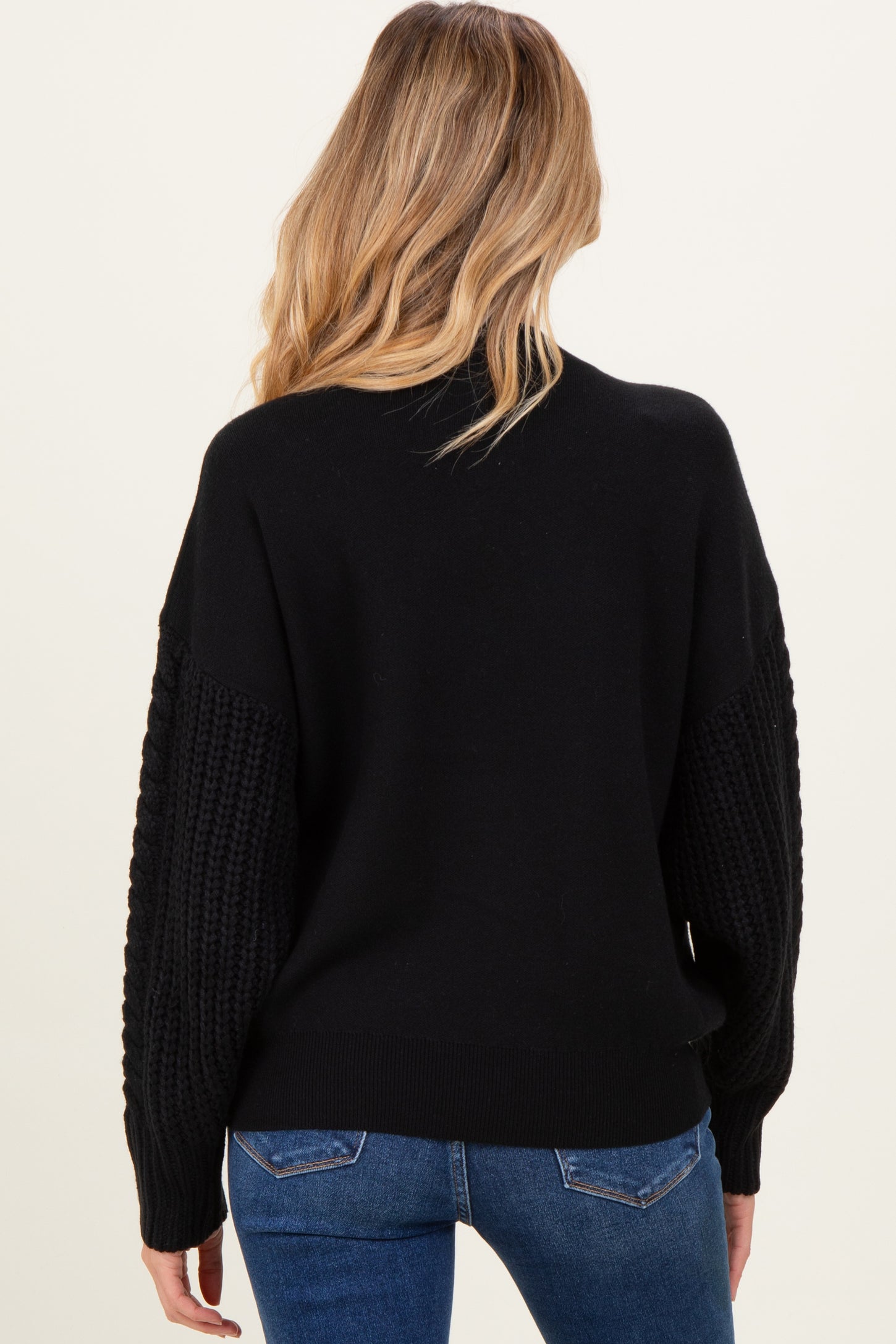 woman wearing a black maternity sweater with textured sleeves and a relaxed fit, viewed from the back