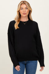 woman wearing a black maternity sweater with cable knit sleeves and fitted body, styled with blue jeans