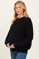 woman wearing a black maternity sweater with cable-knit sleeves and holding her baby bump