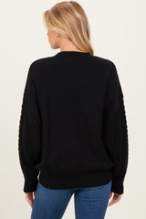 woman wearing a black oversized maternity sweater with textured sleeves and blue jeans