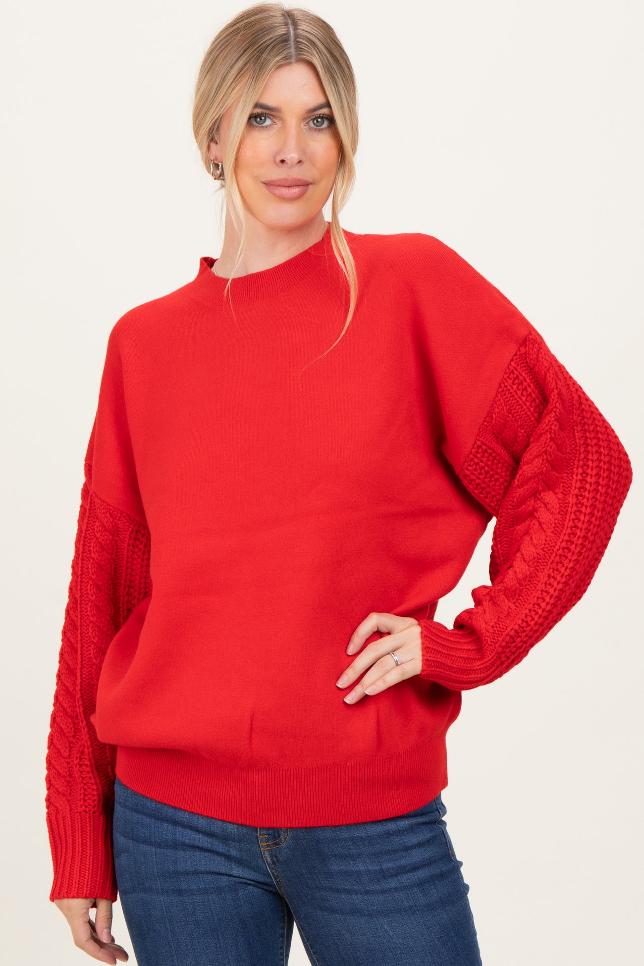 woman wearing a bright red sweater with cable knit sleeves and relaxed fit, paired with blue jeans