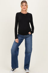 woman wearing a black long sleeve maternity top and blue wide-leg jeans with a visible baby bump