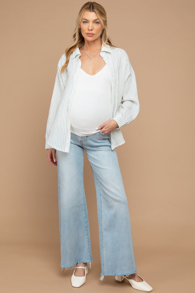 woman wearing a white maternity tank top, striped shirt, and light blue flared jeans, showcasing her baby bump
