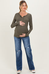 woman wearing a dark green long sleeve maternity top, holding her baby bump, paired with distressed denim jeans