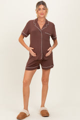 woman wearing a brown maternity short pajama set with white piping, holding her baby bump