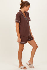 woman wearing a brown short-sleeve pajama set with white piping and shorts, styled with fuzzy slippers