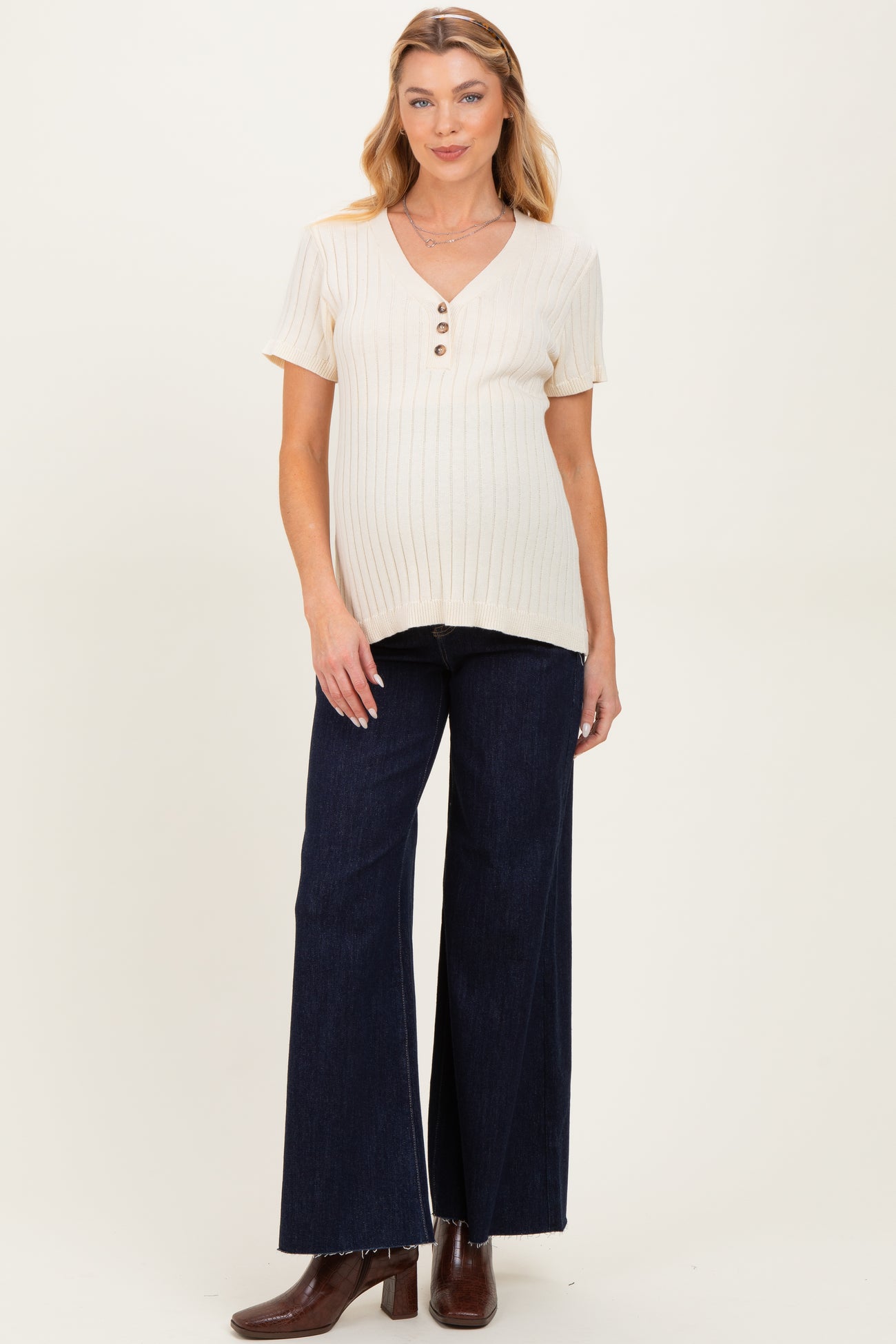 woman wearing a cream v-neck maternity top with buttons and dark blue wide-leg jeans, showing her baby bump