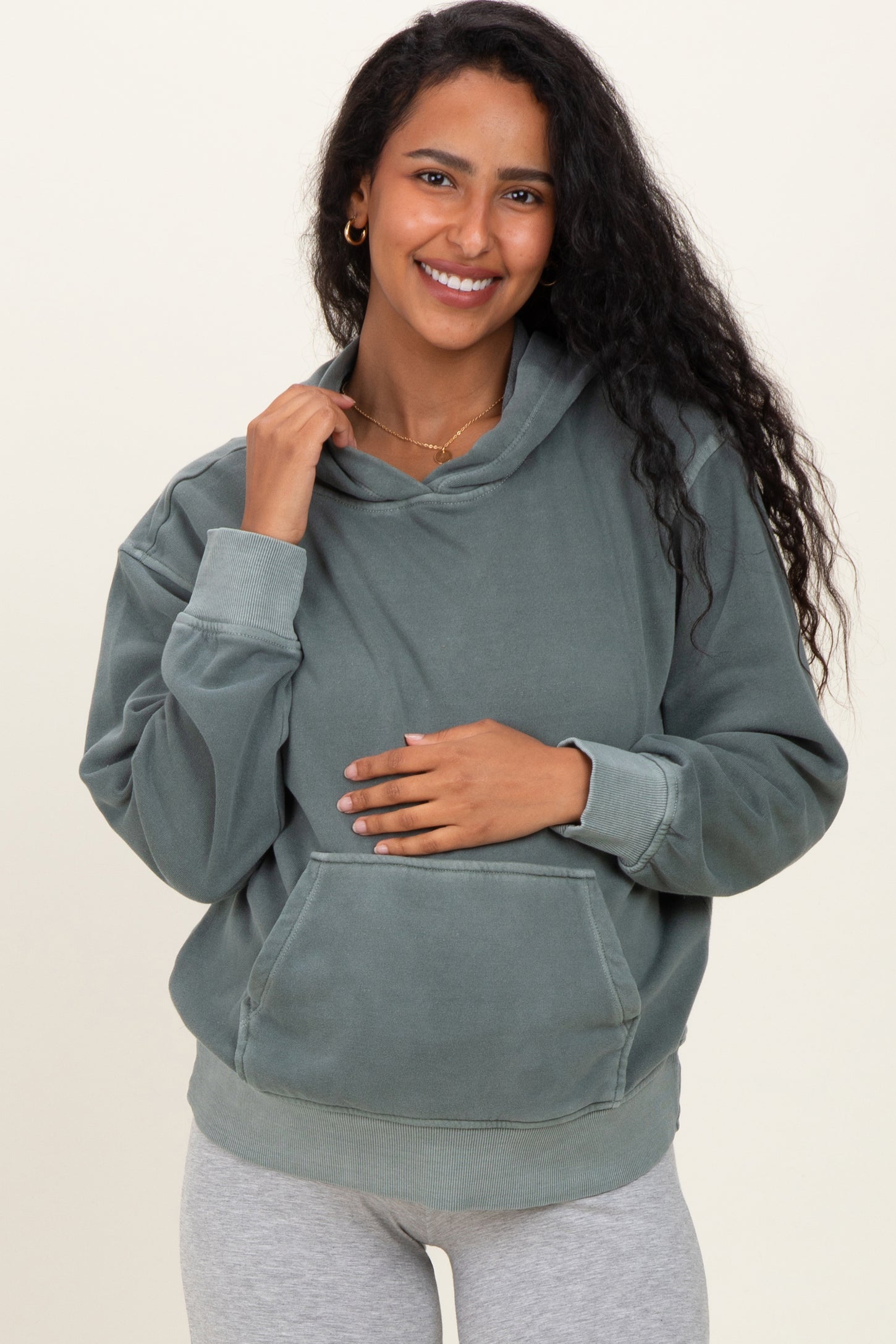 woman wearing a green maternity hoodie with a relaxed fit, holding her baby bump and smiling