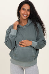 woman wearing a green maternity hoodie with a relaxed fit, holding her baby bump and smiling