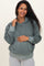woman wearing a green maternity hoodie with a relaxed fit, holding her baby bump and smiling