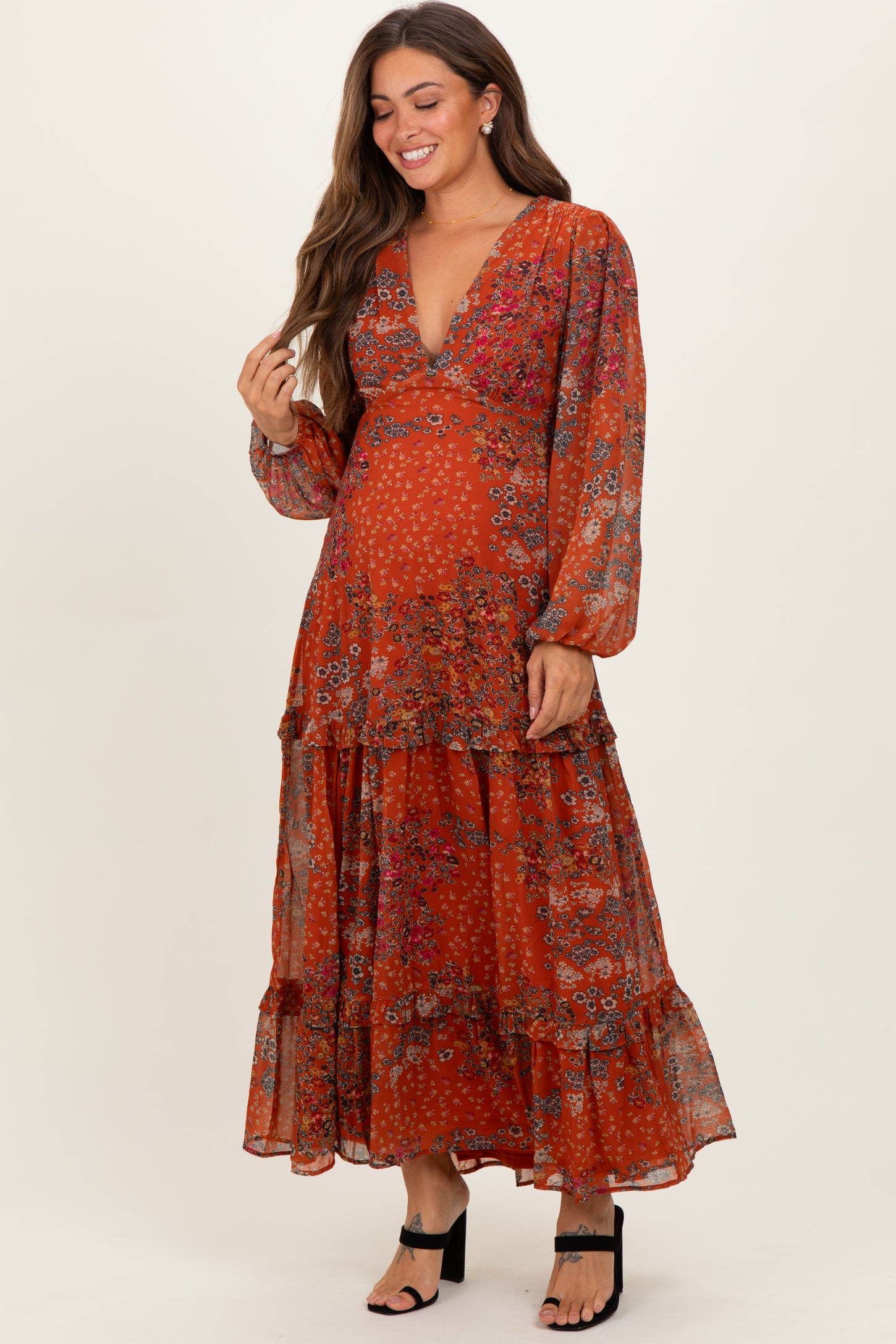 woman wearing an orange floral maternity maxi dress with a deep V-neck and tiered ruffle details, showing her baby bump