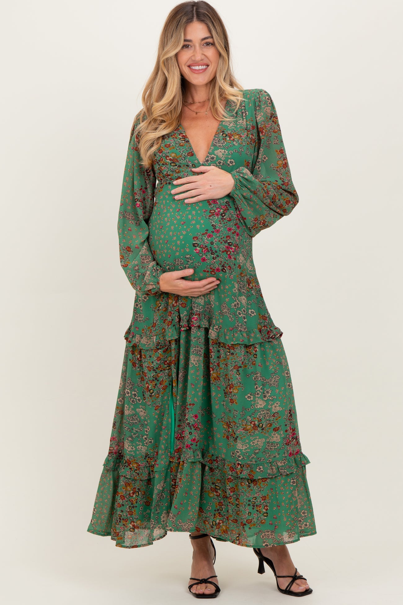 woman wearing a patterned green maternity dress with a deep V-neck and ruffle details, holding her baby bump
