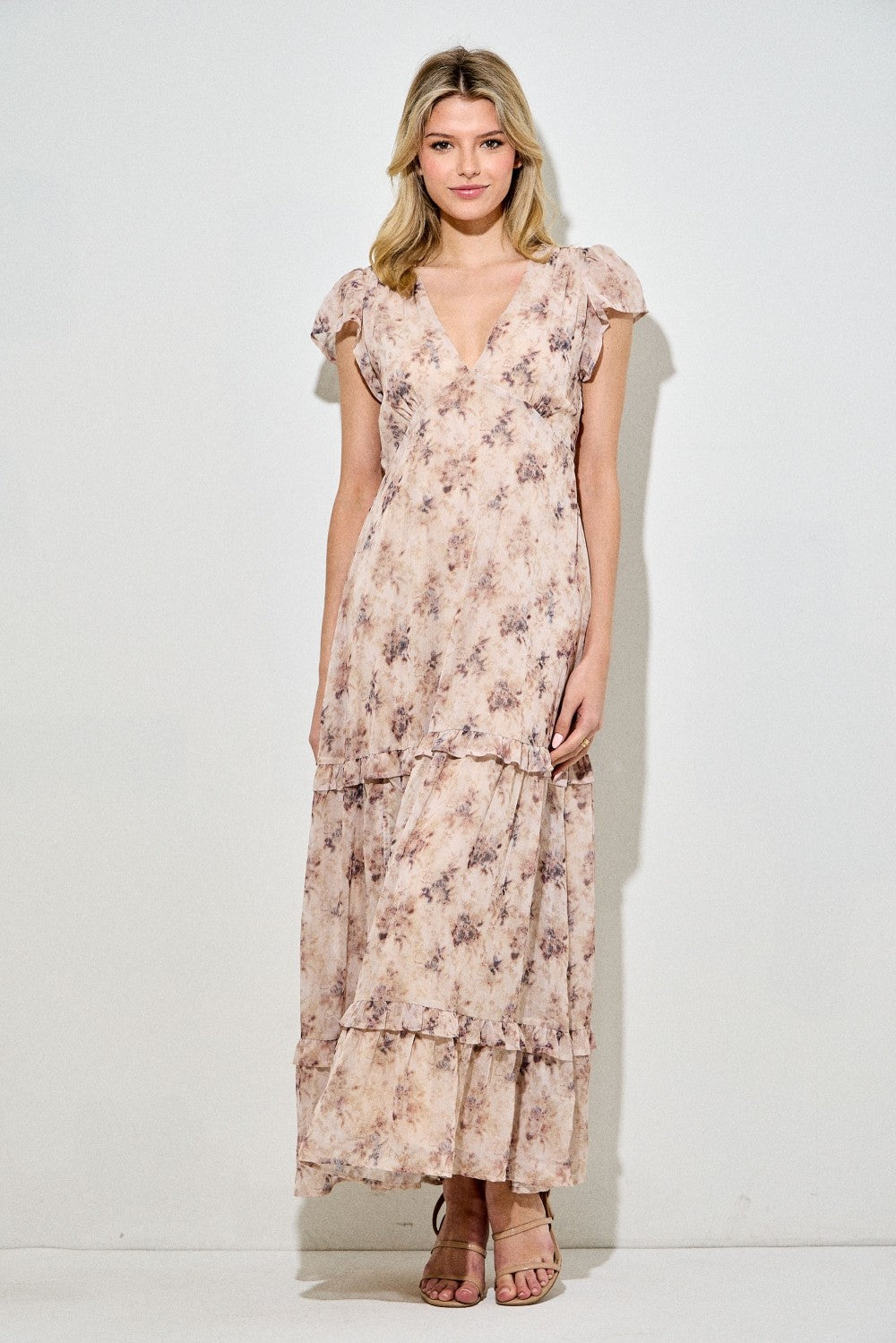 woman wearing a long floral maxi dress with ruffled sleeves and a tiered skirt in soft pastel colors