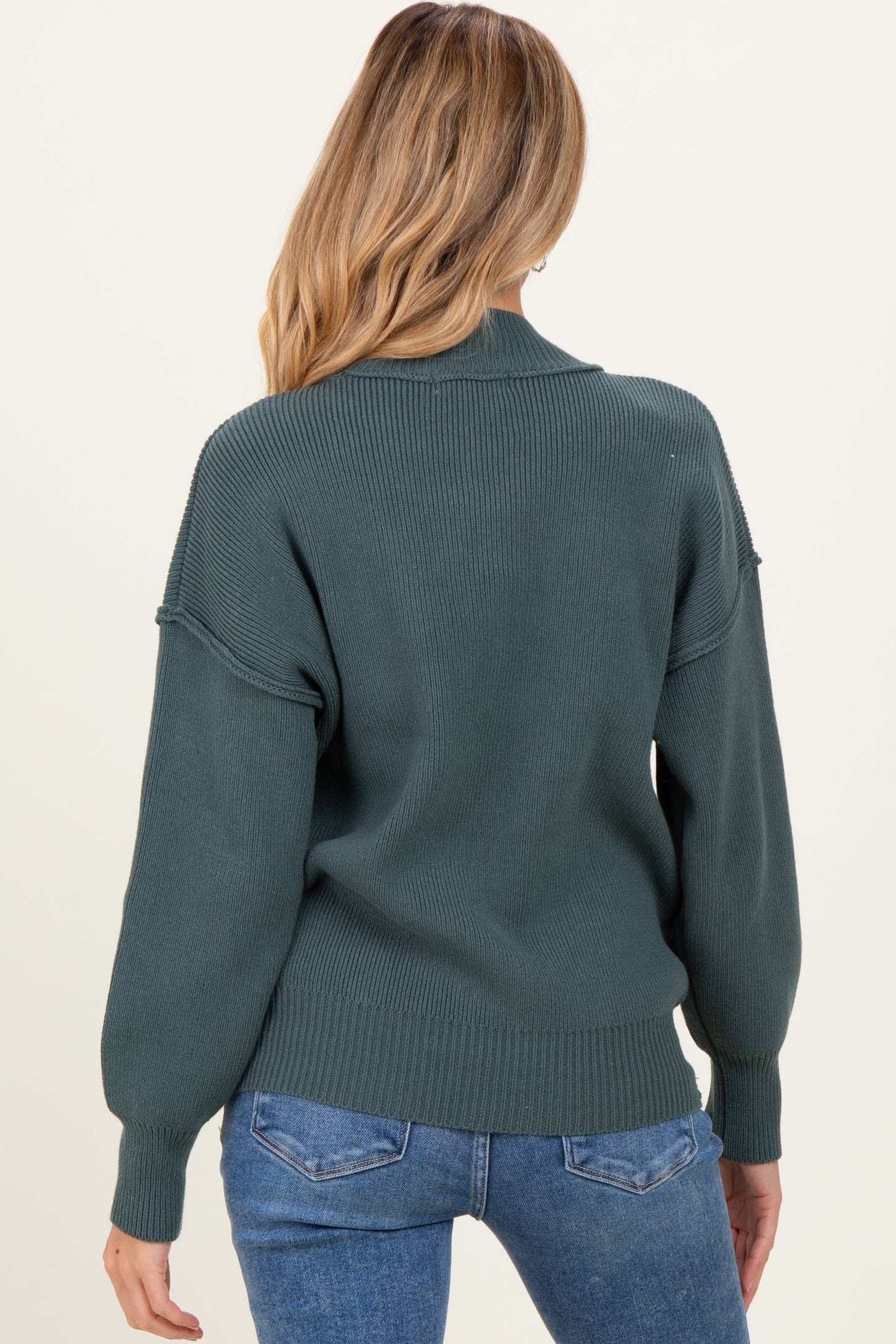 woman wearing a dark green oversized sweater with balloon sleeves, shown from the back