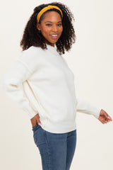 woman wearing a white oversized sweater with ribbed texture and a high neckline paired with blue jeans