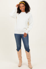 woman wearing a white oversized sweater, blue jeans, and beige knee-high boots, smiling with a yellow headband in her curly hair