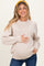woman wearing a light beige oversized maternity sweater, smiling and holding her baby bump