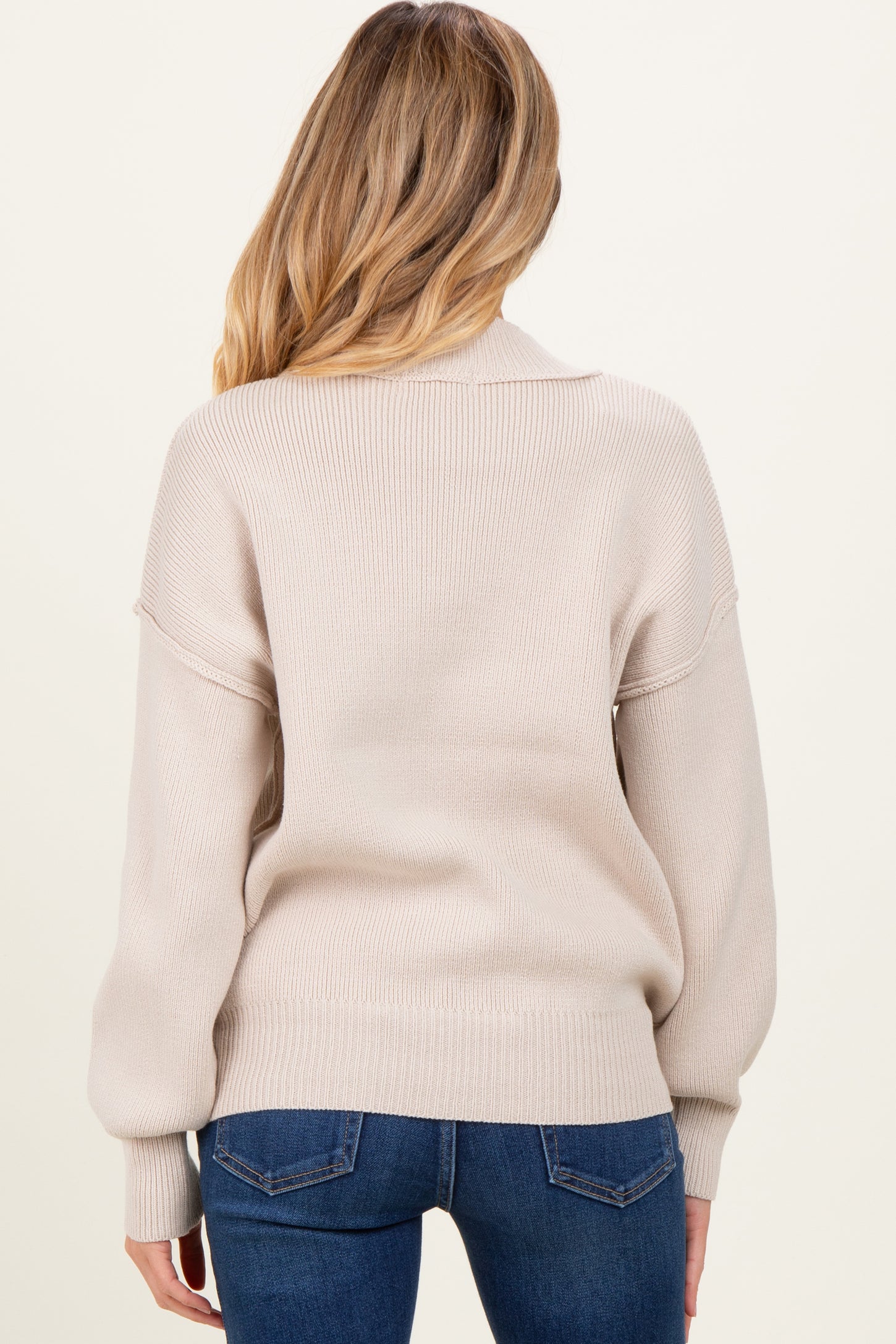 woman wearing a light beige oversized maternity sweater with ribbed texture and balloon sleeves, seen from the back
