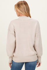 woman wearing a beige oversized knit maternity sweater, view from the back, paired with blue jeans