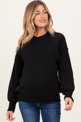 woman wearing a black maternity sweater with long sleeves and a relaxed fit, showing her baby bump