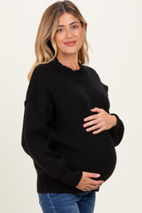 woman wearing a black maternity sweater and cradling her baby bump