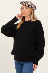 woman wearing a black oversized maternity sweater and blue jeans, with a leopard print beret, and showing her baby bump