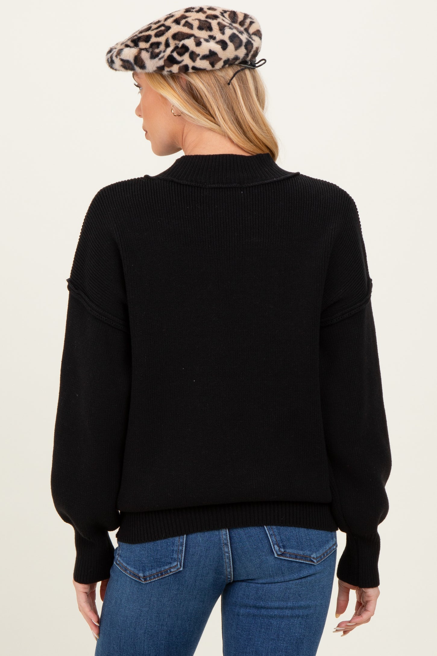 woman wearing a black maternity sweater with balloon sleeves and a high neck, seen from the back