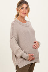 woman wearing a beige knitted maternity sweater and gently cradling her baby bump