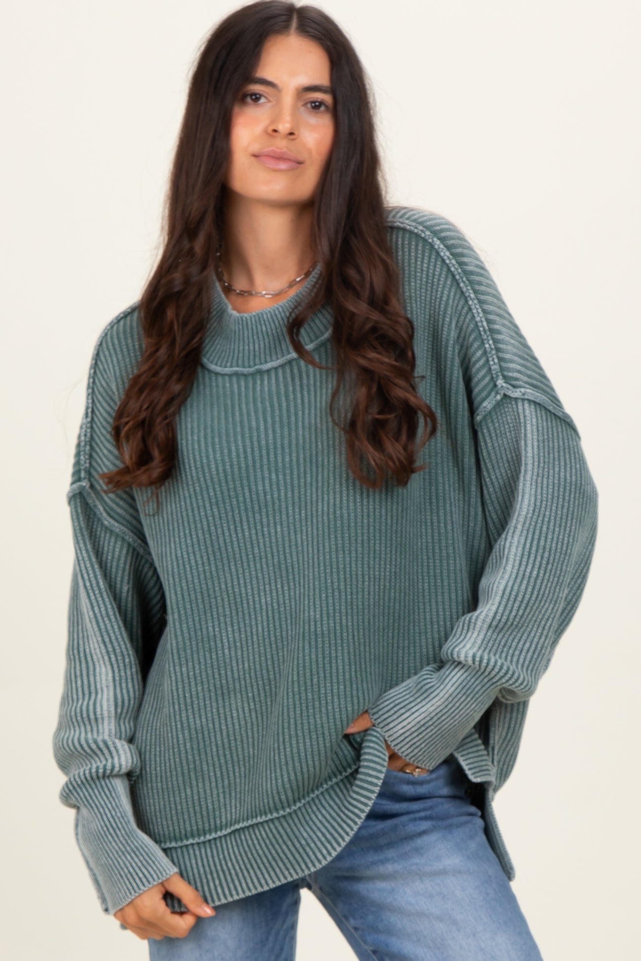 woman wearing a teal oversized ribbed sweater with a mock neck and side slits, paired with light blue jeans