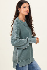 woman wearing a green oversized ribbed sweater with a scooped neckline and side slits, styled with blue jeans