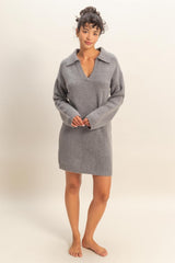 woman wearing a gray sweater dress with a v-neck and collar, standing barefoot against a neutral background
