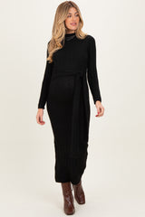 woman wearing a black ribbed maternity maxi dress with a tie waist and long sleeves, showing her baby bump