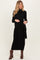 woman wearing a black knitted maternity dress with a tie waist detail and long sleeves, showing her baby bump