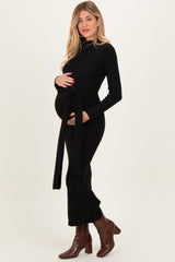 woman wearing a black ribbed maternity dress with a tie waist, showcasing her baby bump