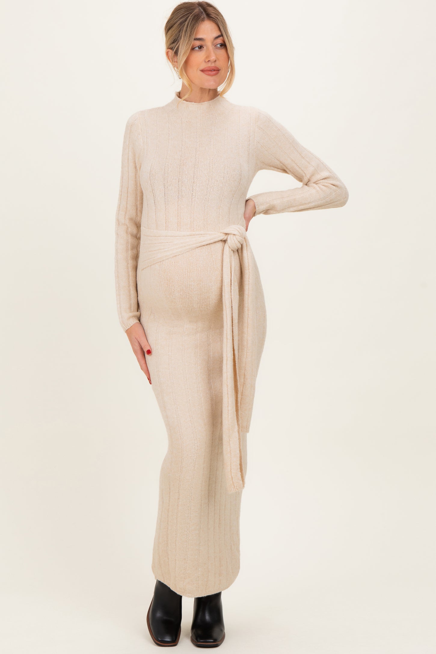 woman wearing a cream long sleeve knitted maternity dress with a tie belt and visible baby bump