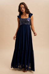 woman wearing a navy blue maxi dress with sequined bodice and ruffled sleeves